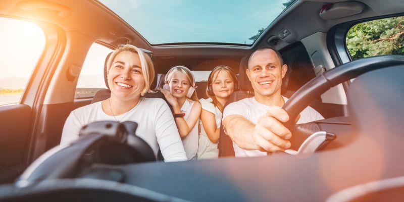 Happy young couple with two daughters inside car during auto trop. They are smiling, laughing during road trip. Family values, traveling concepts.